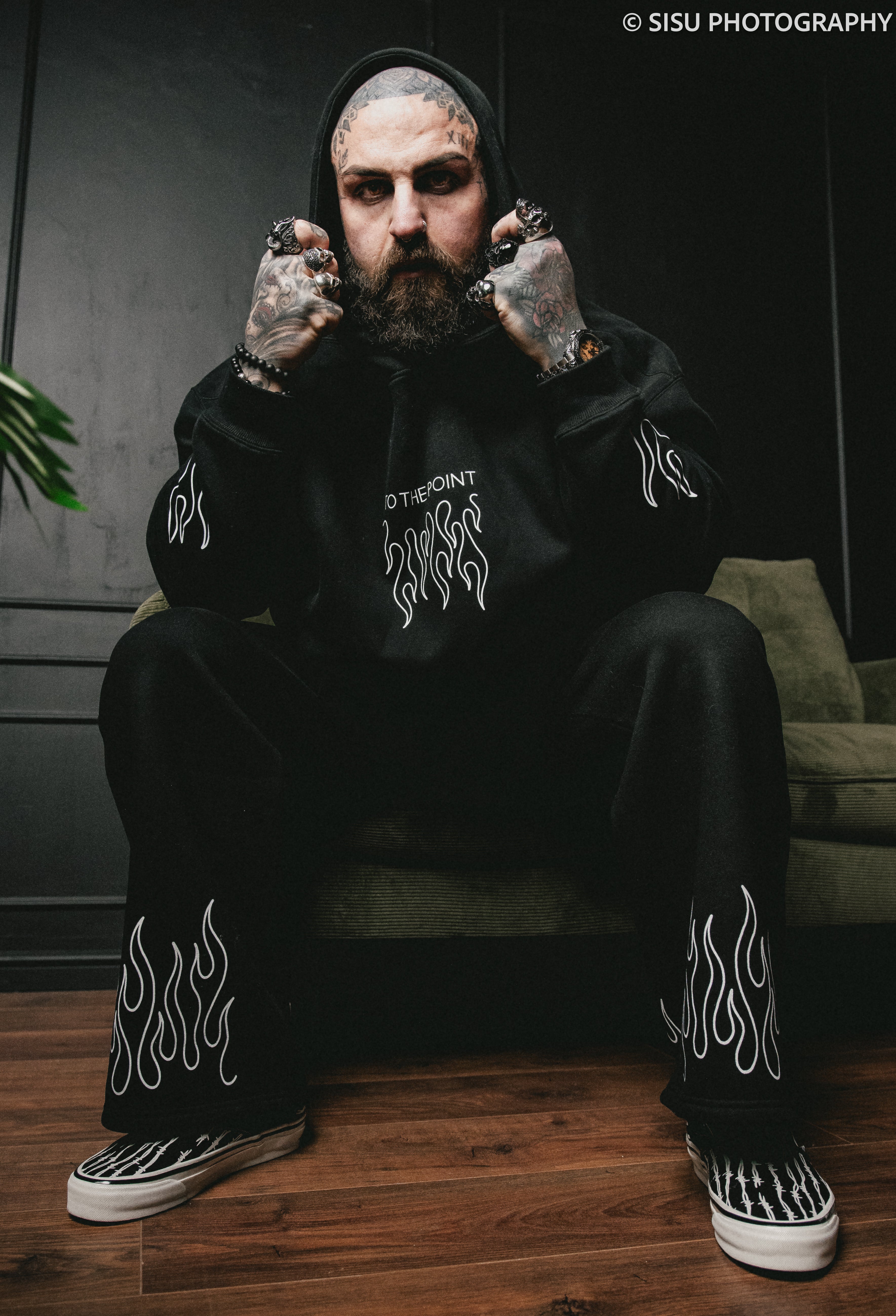 Person wearing a black hoodie with white text and flames, sitting on a couch.
